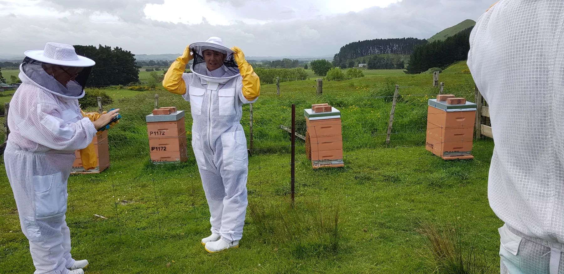 Two women in bee suits in front of some bee hives on a cold and cloudy day