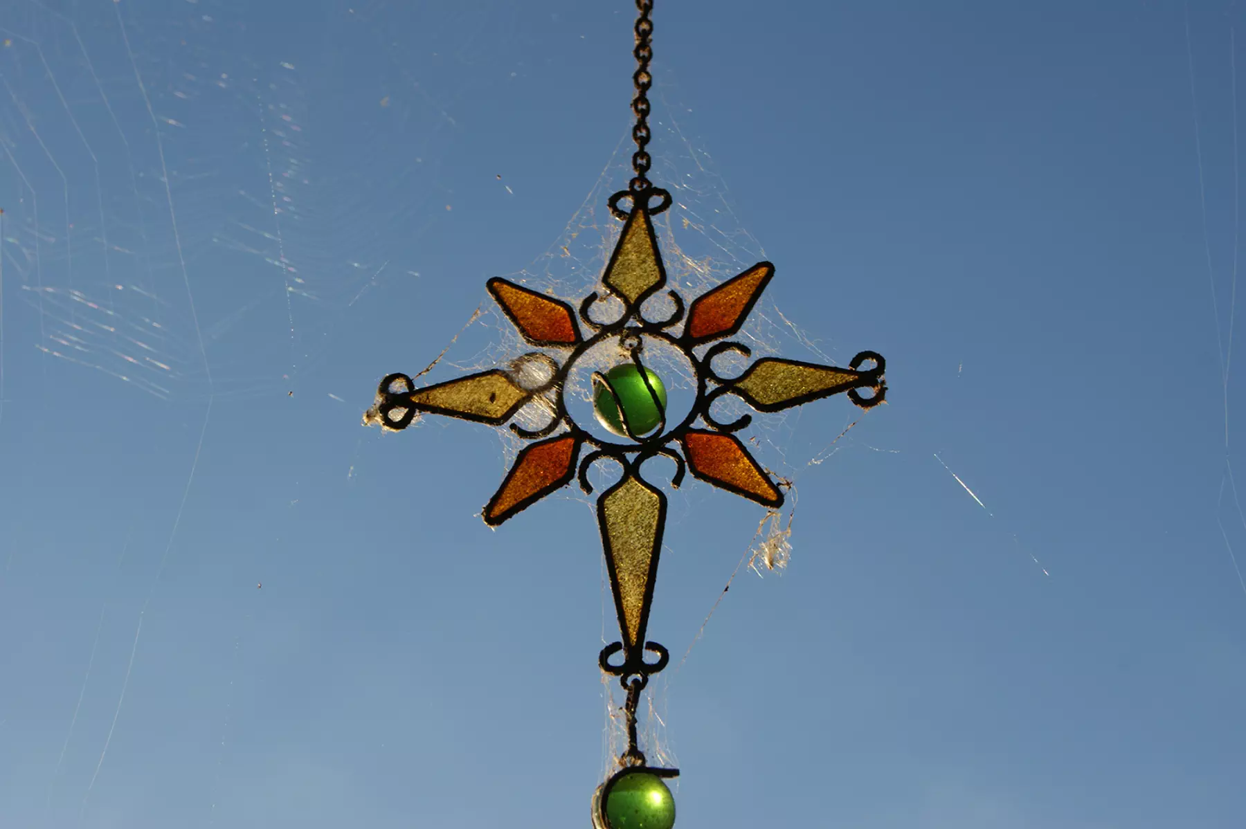 An outside hanging ornament made of coloured glass and marbles covered in spiderwebs